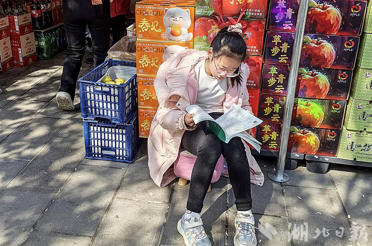  在人来人往喧哗的大街上，有位边看店边看书的少年