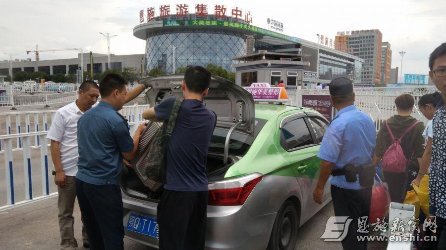 恩施市运管所执法人员维持出租车停靠点秩序，帮助乘客把行李搬上车。